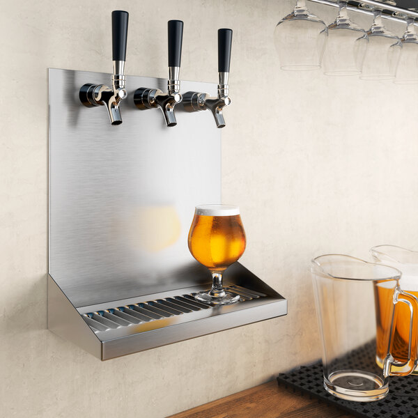 A Regency stainless steel beer drip tray with three beer faucets over a metal shelf with a glass of beer on it.