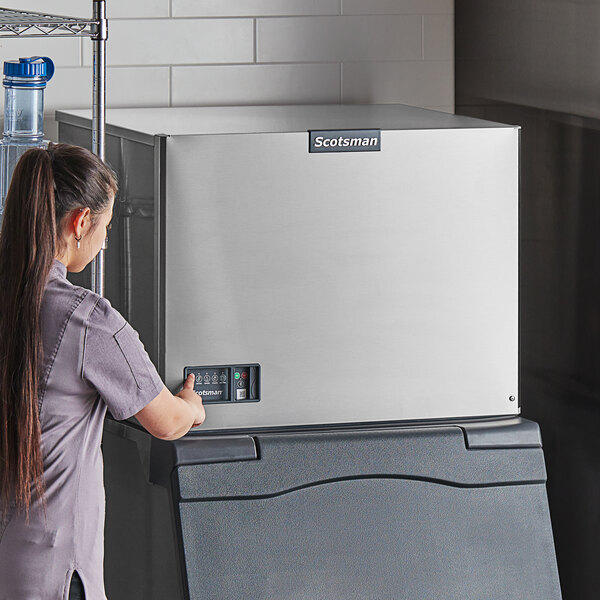 A woman standing next to a large silver Scotsman water cooled ice machine.