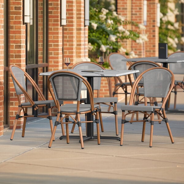 A Lancaster Table and Seating Versilla table with black chairs and a white table top on a patio outside a building.