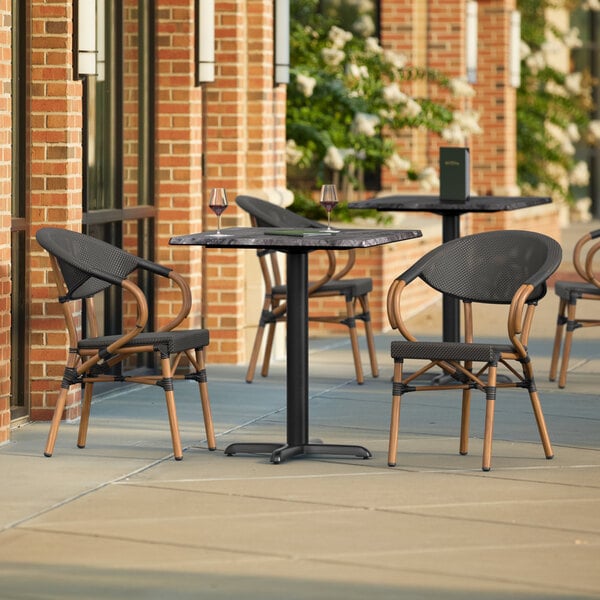 A Lancaster Table & Seating Paladina table with black French bistro chairs on an outdoor patio.