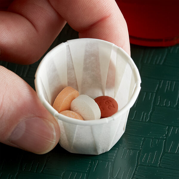 A hand holding a Genpak Harvest .75 oz. paper souffle cup with pills in it.