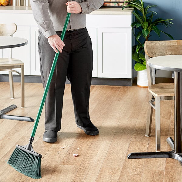A man using a Lavex Green Flagged Angled Broom to sweep the floor in a restaurant.