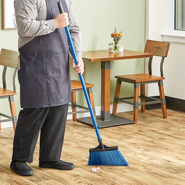 A person using a Lavex blue angled broom with a metal handle to sweep the floor.