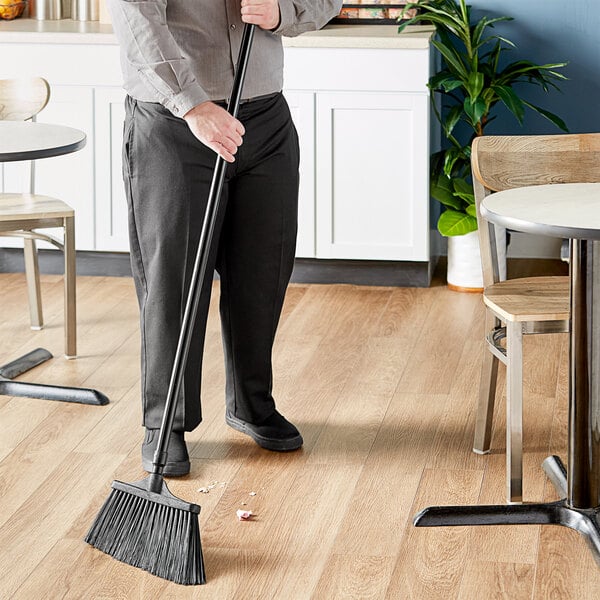 A man using a Lavex angled broom with a black and metal handle to sweep the floor in a professional kitchen.