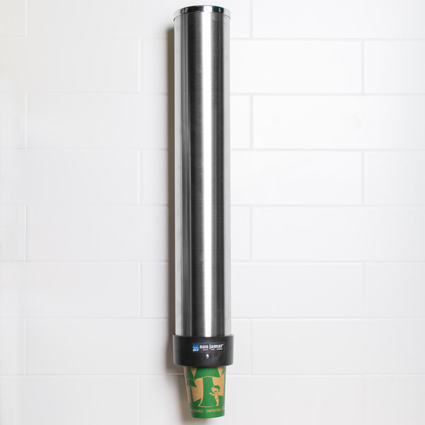A San Jamar stainless steel cup dispenser attached to a wall with a green cup on it.