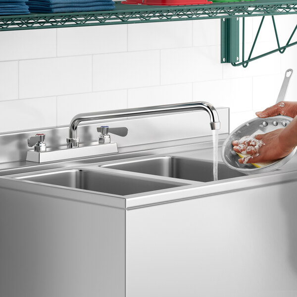 A person washing dishes in a stainless steel sink using a Regency deck-mounted faucet.