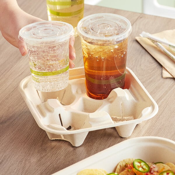 A hand holding a World Centric compostable drink carrier with four plastic cups of soda.