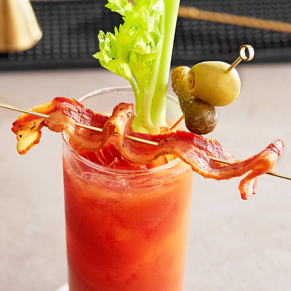 A bloody mary with bacon and celery on a table with a yellow raspberry chipotle bacon toothpick.