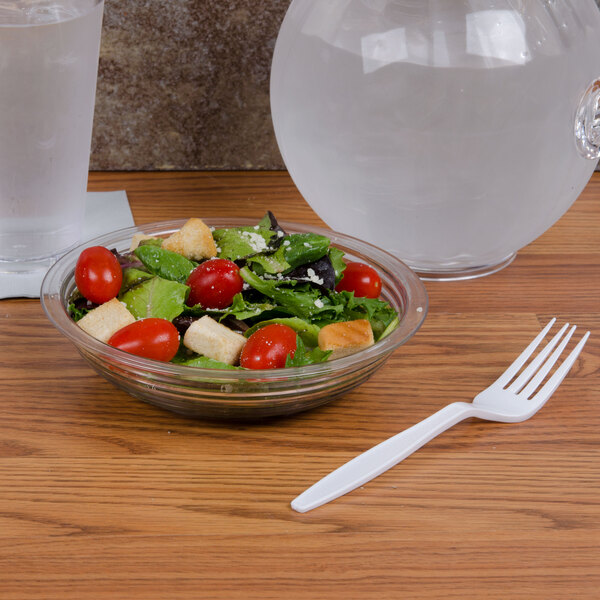 A bowl of salad with tomatoes and croutons on a white table next to a plastic fork.