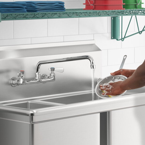 A person washing dishes in a sink with a Regency wall mount faucet.