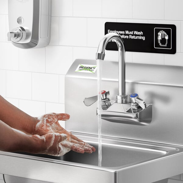 A person washing their hands under a Regency wall mount faucet.