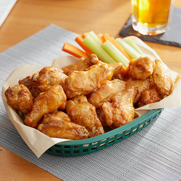A basket of chicken wings and vegetables on a table.