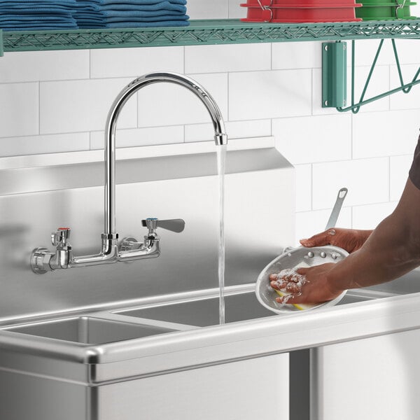 A man washing dishes in a sink using a Regency wall mount faucet.