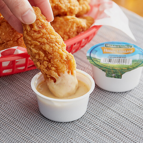 A person dipping a piece of fried chicken into a cup of Hidden Valley Golden Honey Mustard Dressing.
