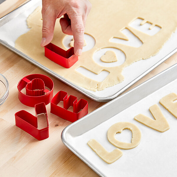 A person using Wilton L-O-V-E cookie cutters to make cookies.