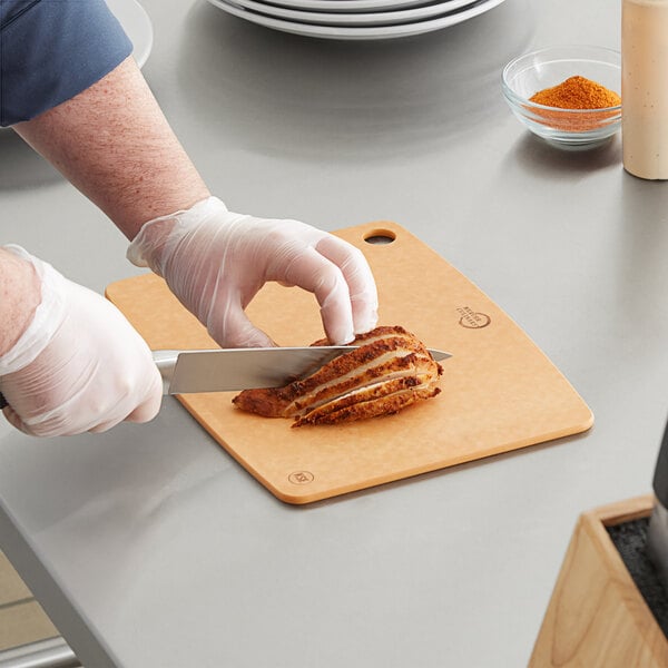 A person cutting a piece of meat on a Mercer cutting board.