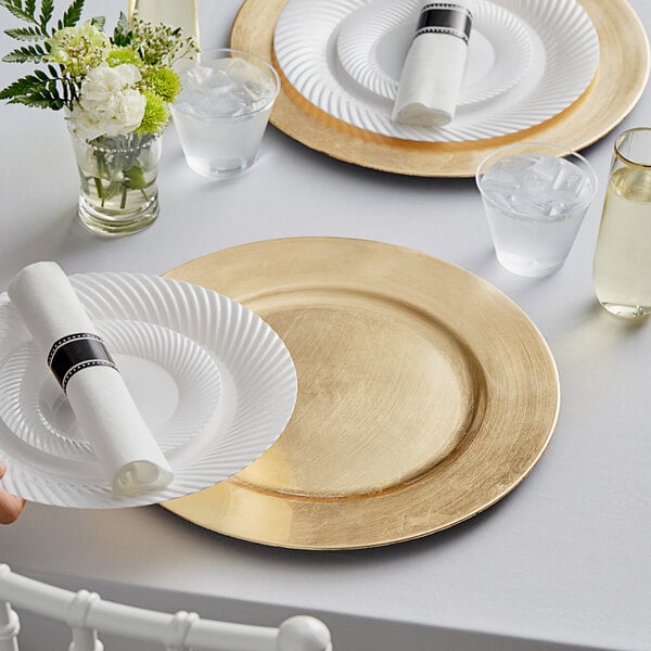 A hand holding a Choice gold charger plate with a white napkin on top.