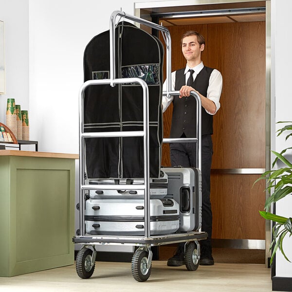 A man in a suit and tie pushing a Lancaster Table & Seating stainless steel bellman cart.