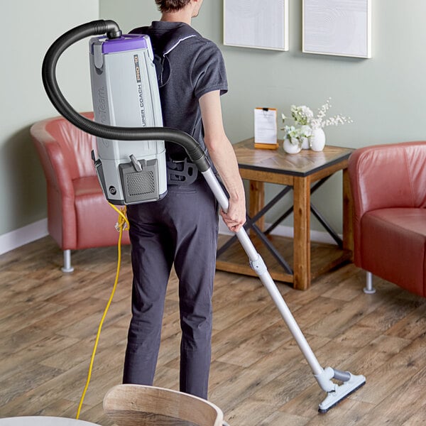 A man using a ProTeam backpack vacuum to clean a wood floor.