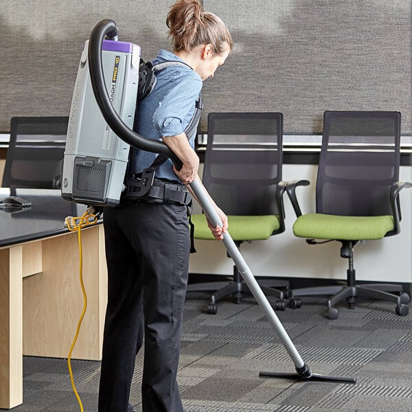 A woman using a ProTeam backpack vacuum to clean an office floor.