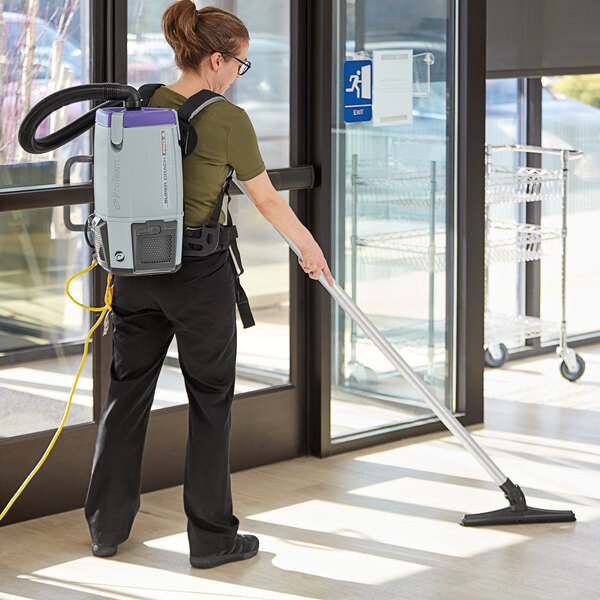 A woman using a ProTeam Super Coach Pro backpack vacuum to clean a building.