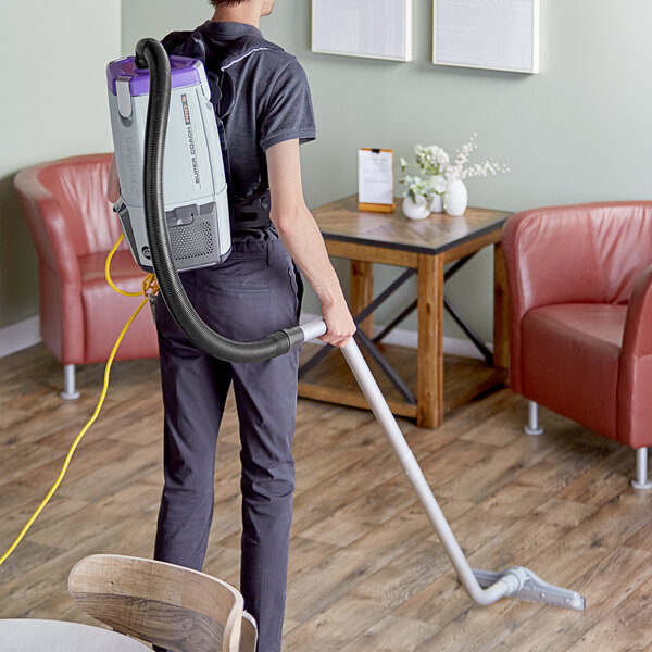 A person using a ProTeam backpack vacuum to clean a room.