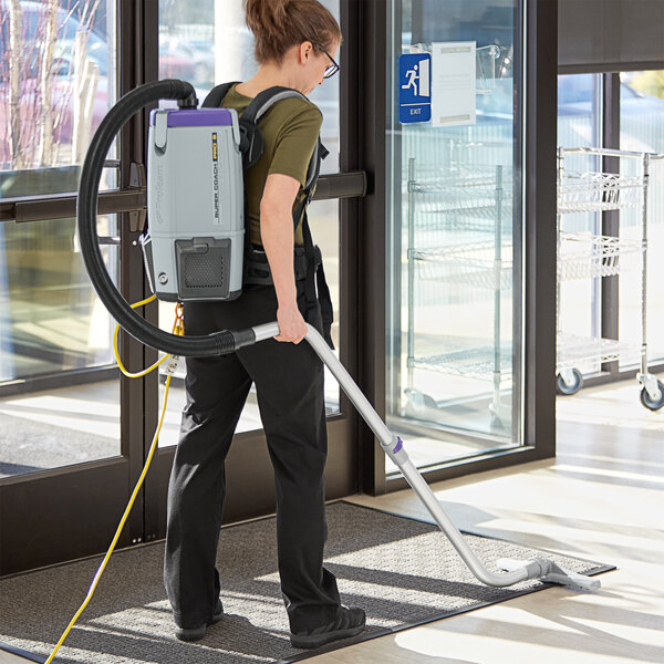 A woman using a ProTeam backpack vacuum to clean a building.