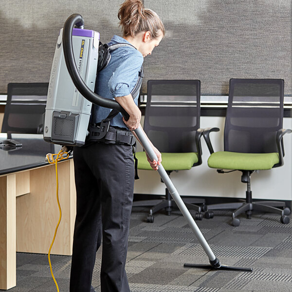 A woman using a ProTeam backpack vacuum to clean a green office chair.