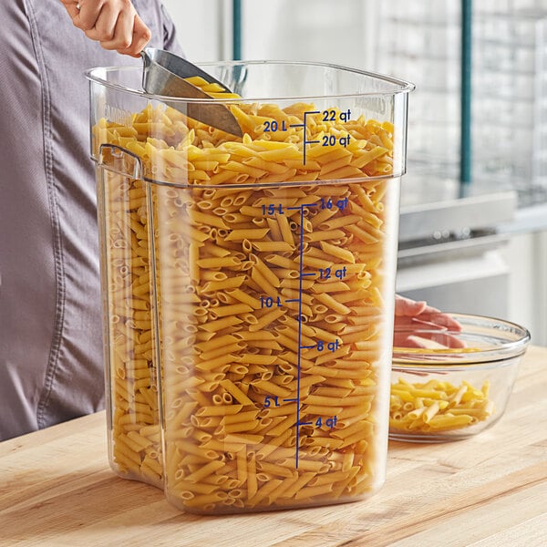 A woman cutting pasta in a large Cambro container on a counter in a home kitchen.