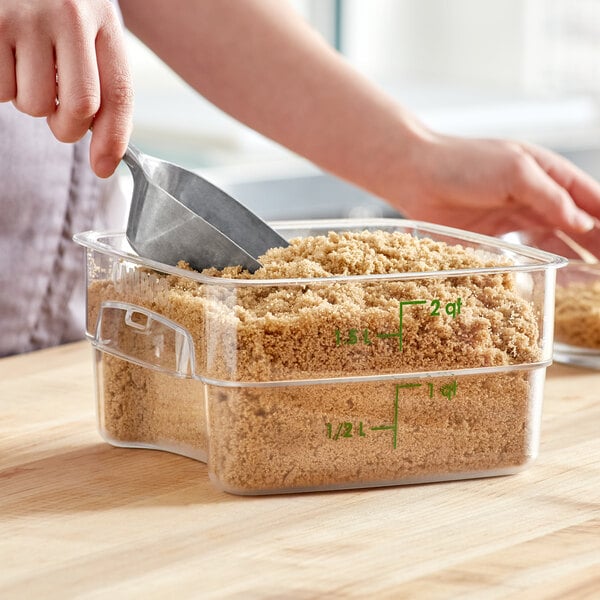 A person using a scoop to scoop brown sugar into a Cambro food storage container.