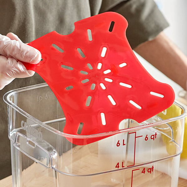 A gloved hand placing a red Cambro FreshPro polypropylene container in a red polypropylene drain tray on a kitchen counter.
