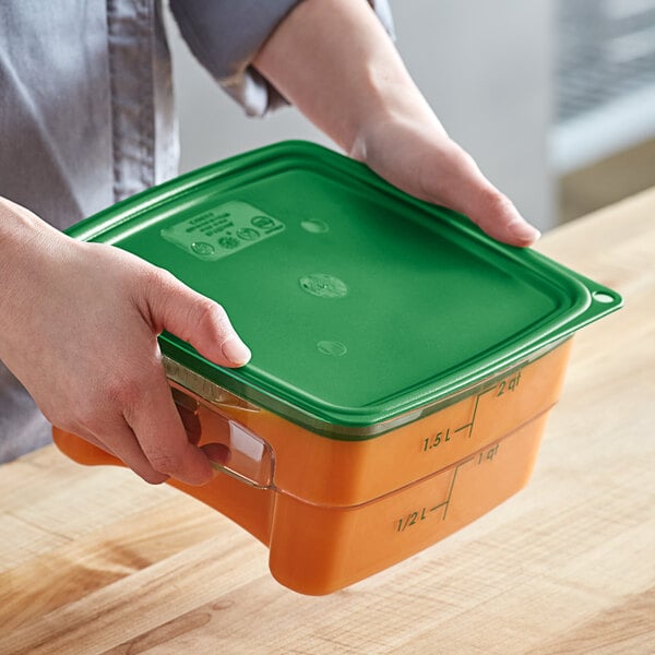 A person holding a Cambro green square polypropylene food storage container with a green lid.