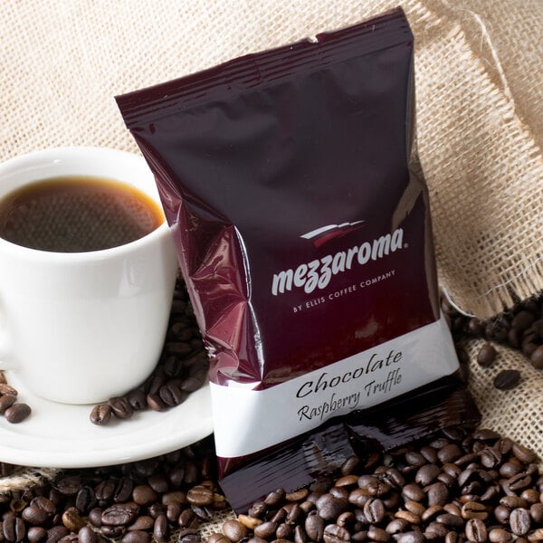 A Ellis Mezzaroma Chocolate Raspberry Truffle coffee packet next to a cup of coffee.