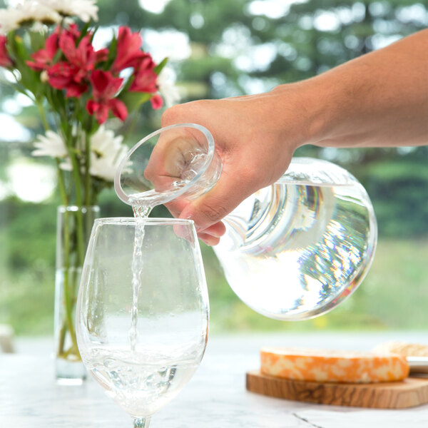 A hand pouring water from a Stolzle glass carafe into a wine glass.