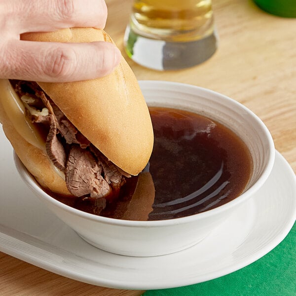 A person holding a sandwich in a bowl of au jus.