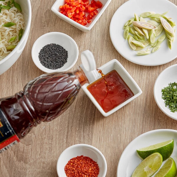 A bottle of THAI Kitchen fish sauce pouring into a bowl of noodles with green onions and red peppers.