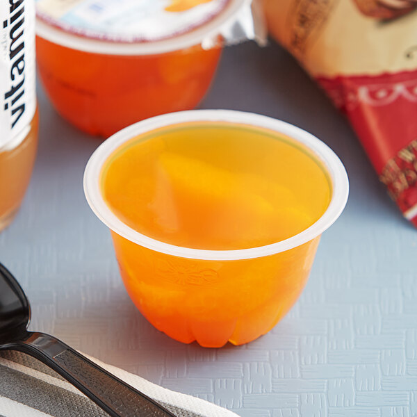 A plastic cup of Dole Mandarin oranges in orange flavored gel with a spoon next to it.