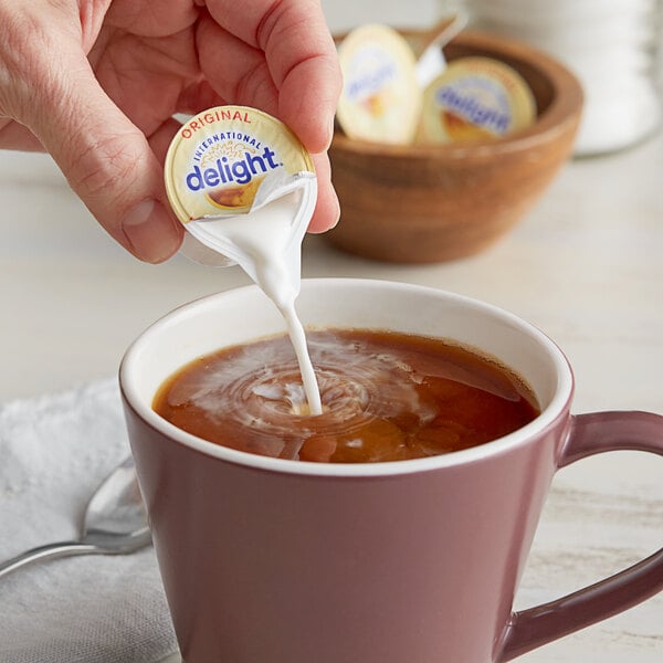 A person pouring International Delight creamer into a cup of coffee.
