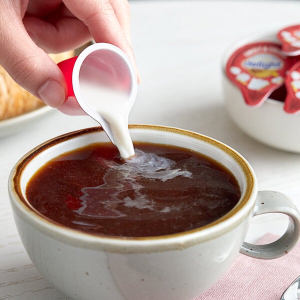 A person pouring International Delight Sweet & Creamy non-dairy creamer into a cup of coffee.