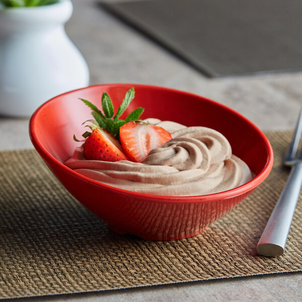 A close up of a red GET Red Sensation slanted bowl filled with chocolate dessert topped with strawberries.