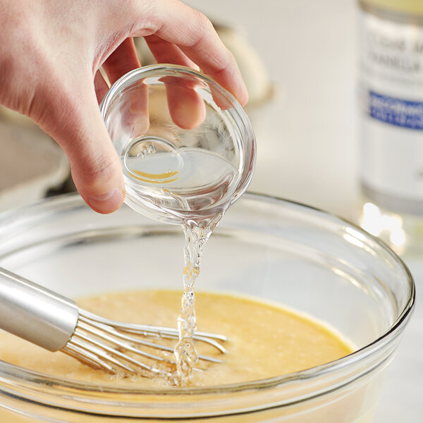 A person pouring McCormick Culinary Clear Imitation Vanilla into a bowl of liquid on a counter in a professional kitchen.