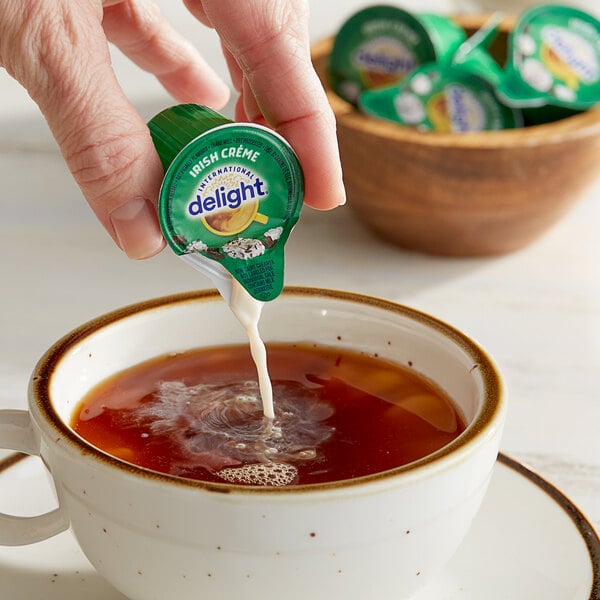 A hand pouring International Delight Irish Creme creamer from a small green container into a cup of tea.