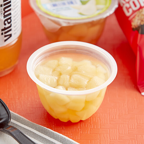 A plastic container of Dole diced pears in juice with a spoon on a table.