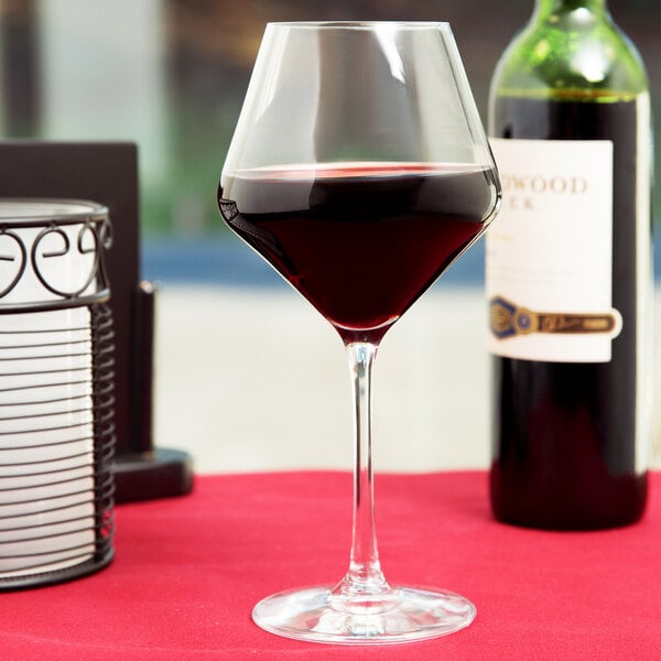 A Stolzle burgundy wine glass filled with red wine on a table.