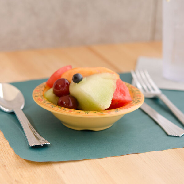 A bowl of fruit on a table with a fork and spoon.