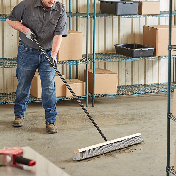 A man using a Lavex push broom with a metal handle to sweep the floor.
