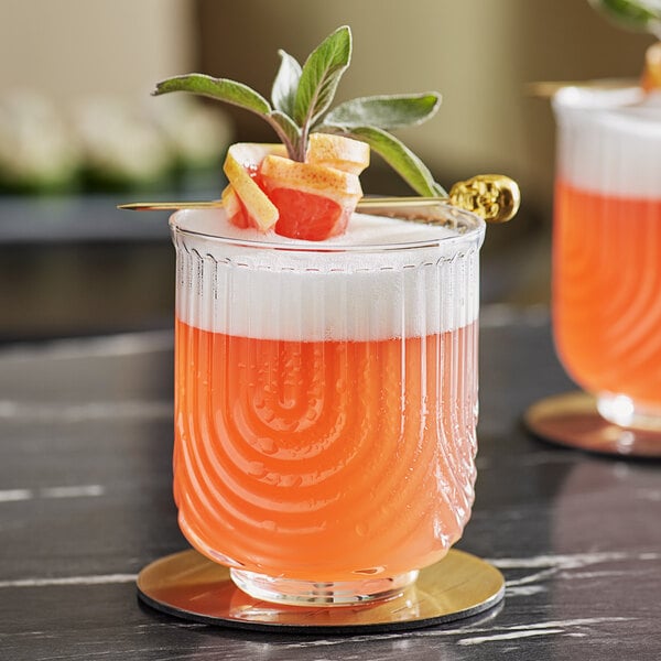 A close up of two Acopa Zelda double old fashioned glasses filled with orange drinks and garnished with fruit.