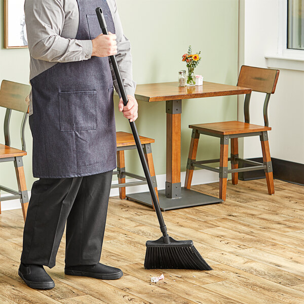 A person sweeping a floor with a Lavex black angled broom with a black metal pole.