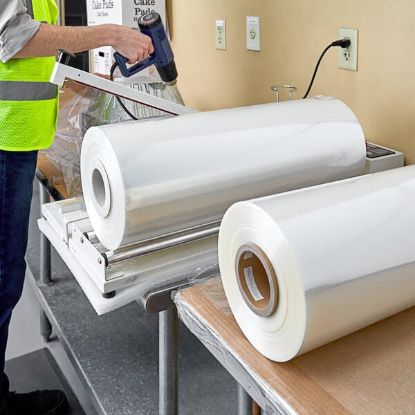 A person in a yellow vest using a machine to wrap a roll of Lavex Pro 60 gauge shrink film.