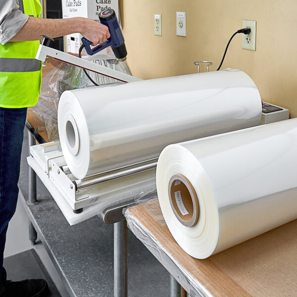 A person in a yellow vest using a machine to roll Lavex Pro cross-linked perforated shrink film.